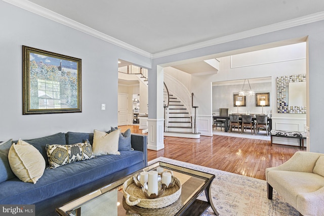 living area featuring wood finished floors, crown molding, stairway, a chandelier, and wainscoting
