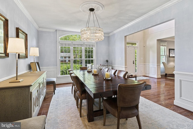 dining space with a chandelier, dark wood finished floors, ornamental molding, wainscoting, and a decorative wall