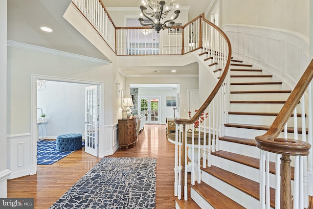 foyer featuring stairway, wood finished floors, a chandelier, a wainscoted wall, and ornamental molding