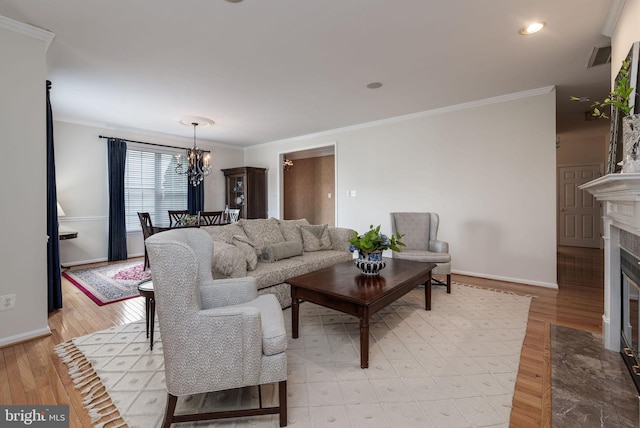living area featuring a chandelier, light wood-style flooring, crown molding, baseboards, and a fireplace with flush hearth
