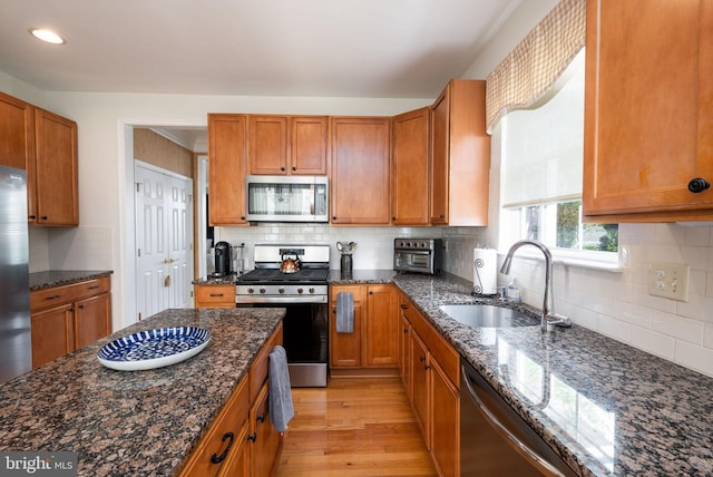 kitchen with appliances with stainless steel finishes, a sink, backsplash, light wood finished floors, and recessed lighting