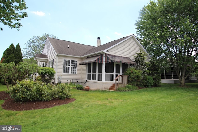 back of property with a chimney, a lawn, a sunroom, and roof with shingles