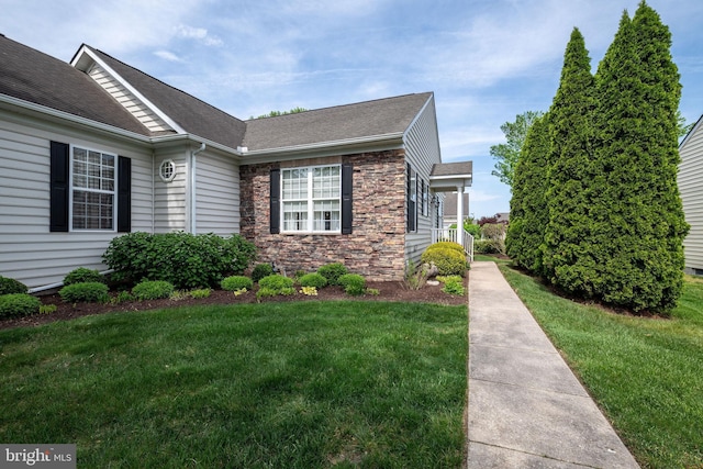 view of front of house with a front yard, stone siding, and roof with shingles