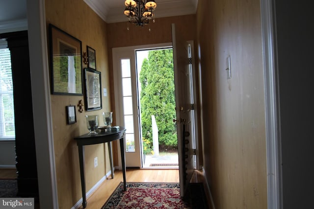 doorway with a chandelier, light wood-type flooring, crown molding, and baseboards