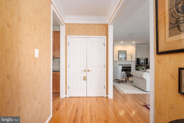 corridor featuring light wood finished floors, ornamental molding, wallpapered walls, and baseboards