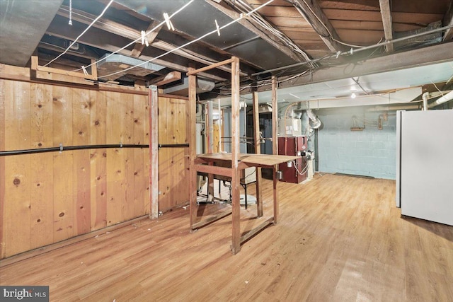 unfinished basement featuring freestanding refrigerator, wood finished floors, and concrete block wall