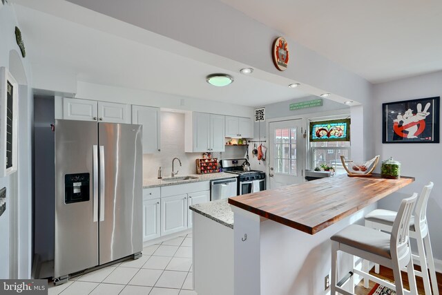 409 Academy Rd, Baltimore, MD 21228 - kitchen with appliances with stainless steel finishes, a sink, butcher block countertops, a breakfast bar area, and light tile patterned floors