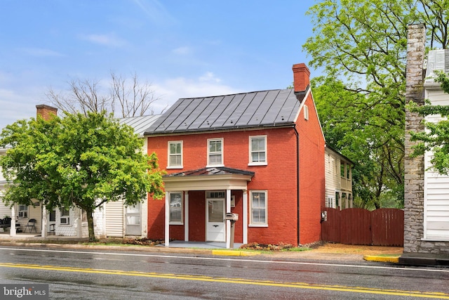multi unit property featuring a standing seam roof, brick siding, fence, and a chimney