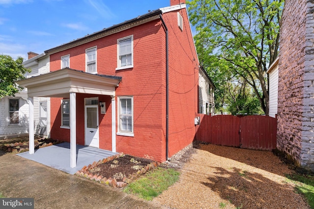 back of property featuring brick siding, a chimney, a gate, and fence