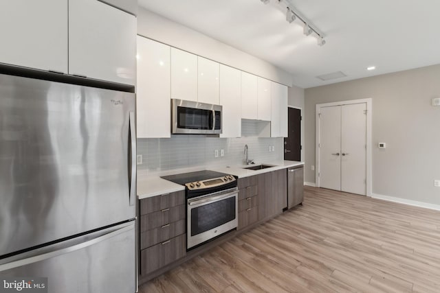 kitchen featuring appliances with stainless steel finishes, modern cabinets, a sink, white cabinetry, and light countertops
