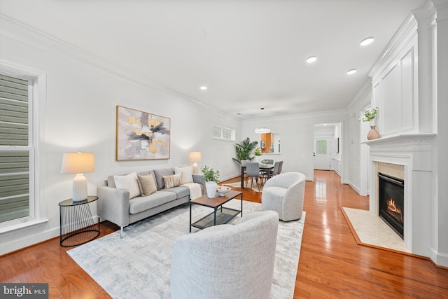 living room featuring a premium fireplace, crown molding, light wood finished floors, baseboards, and recessed lighting