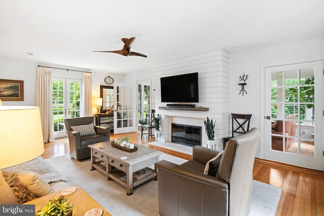 living area with plenty of natural light, light wood-style floors, crown molding, and a glass covered fireplace