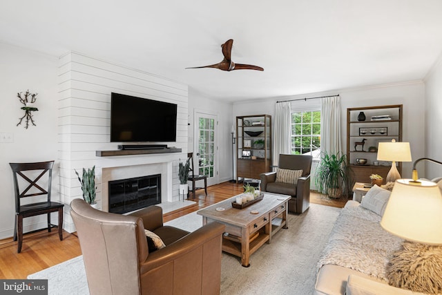 living area with ceiling fan, light wood-style floors, a fireplace, and crown molding