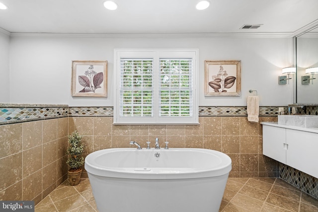 bathroom featuring tile walls, a freestanding tub, crown molding, vanity, and recessed lighting