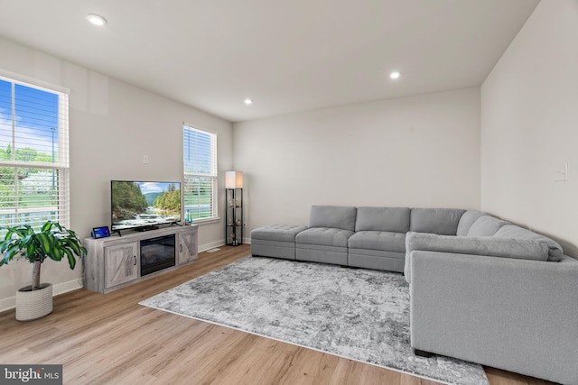 living room featuring baseboards, light wood finished floors, a glass covered fireplace, and recessed lighting