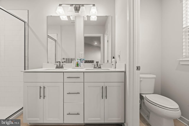bathroom featuring double vanity, toilet, a tile shower, and a sink