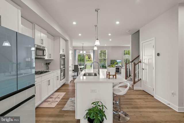kitchen with appliances with stainless steel finishes, a breakfast bar area, recessed lighting, a sink, and light wood-type flooring