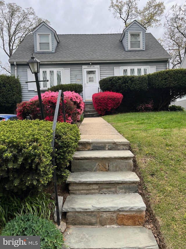 new england style home featuring roof with shingles and a front yard