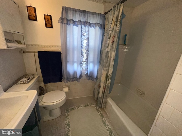 bathroom featuring tile walls, toilet, shower / bath combo with shower curtain, tile patterned flooring, and a sink
