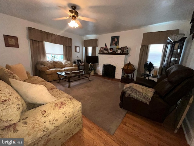 living room with a ceiling fan, a brick fireplace, and wood finished floors