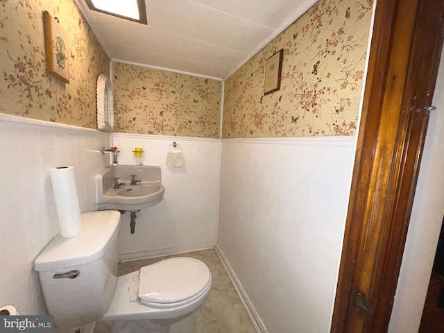 half bath with wainscoting, toilet, and wallpapered walls