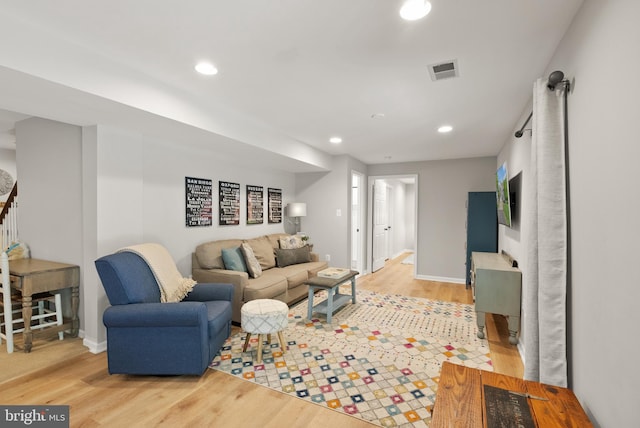 living room featuring stairs, baseboards, visible vents, and light wood-style floors
