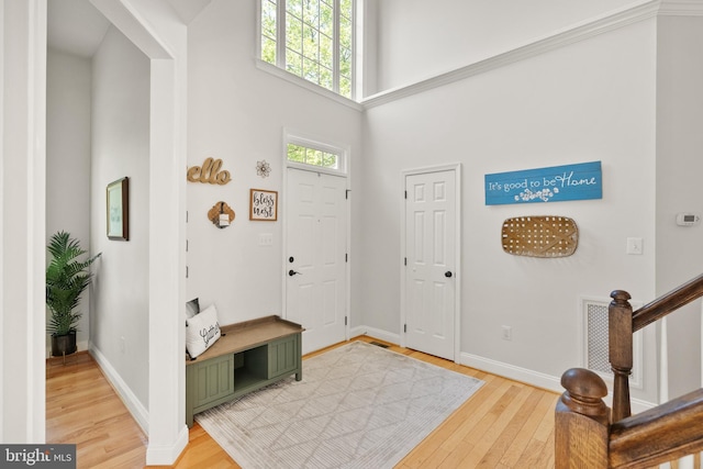 entrance foyer with light wood-style flooring, stairs, baseboards, and a high ceiling