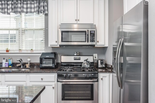 kitchen with stainless steel appliances, white cabinets, a sink, and dark stone countertops