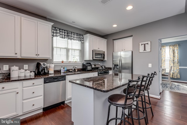 kitchen with appliances with stainless steel finishes, a sink, white cabinets, recessed lighting, and a breakfast bar area