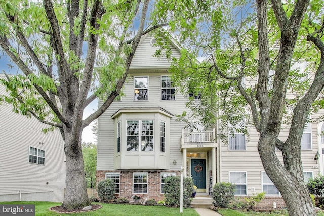 view of front of house with a balcony, brick siding, and a front lawn