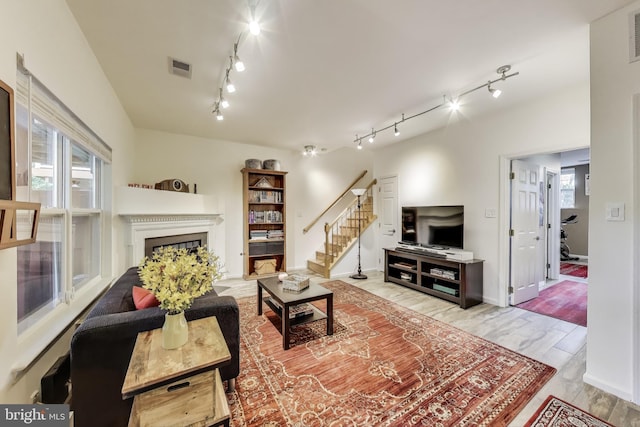 living room featuring stairway, rail lighting, a fireplace, and visible vents
