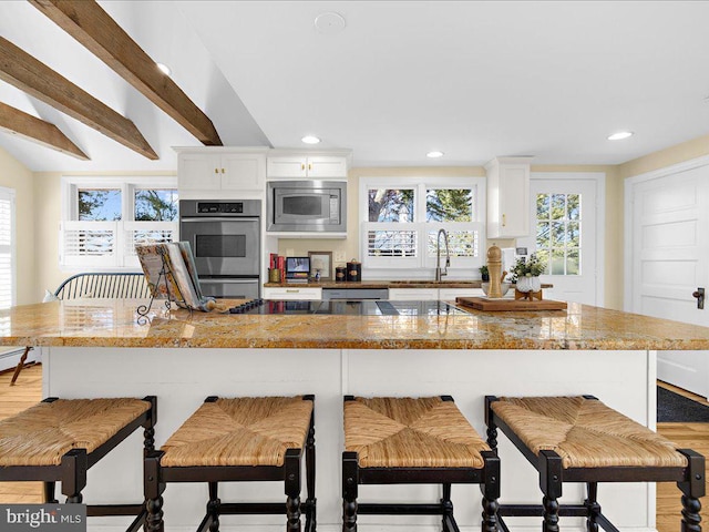 kitchen with a sink, stainless steel appliances, white cabinets, a breakfast bar, and recessed lighting