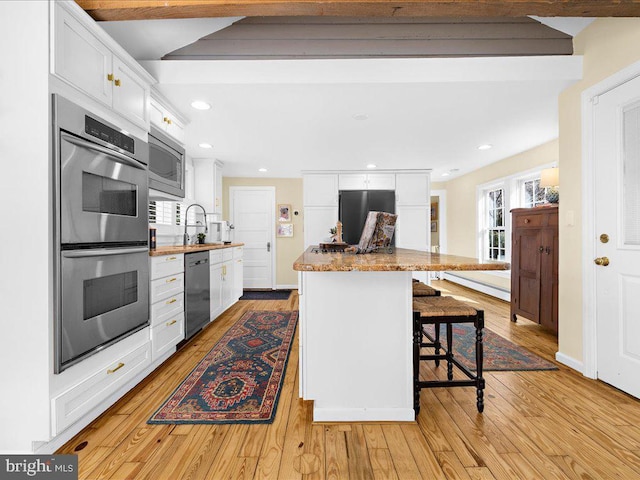 kitchen with stainless steel appliances, white cabinetry, light wood-style flooring, a kitchen bar, and recessed lighting