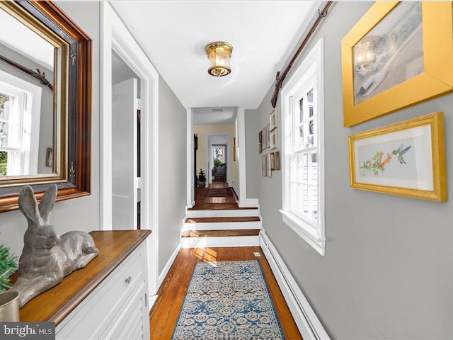 corridor with wood finished floors, a baseboard radiator, baseboards, and stairs