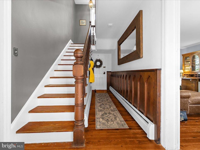 stairway with a baseboard heating unit and wood finished floors