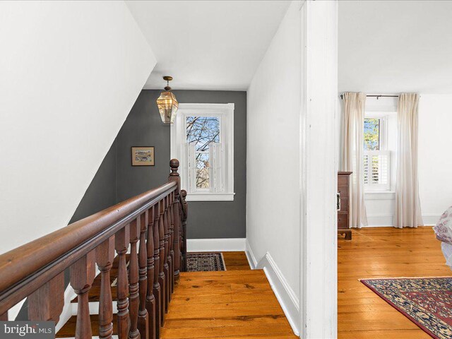 hall with plenty of natural light, wood finished floors, an upstairs landing, and a chandelier
