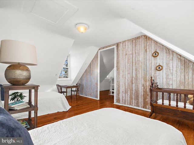 bedroom with lofted ceiling, wood finished floors, wood walls, and attic access