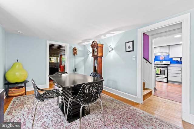 dining area featuring light wood-type flooring, baseboards, and stairs