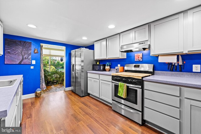kitchen featuring appliances with stainless steel finishes, under cabinet range hood, wood finished floors, a sink, and light countertops