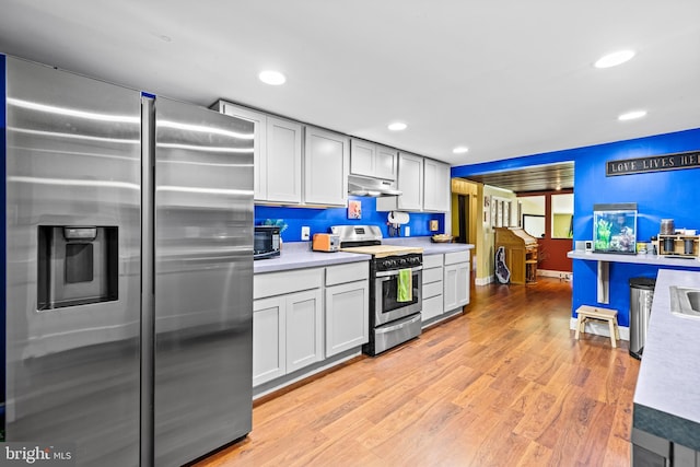 kitchen featuring appliances with stainless steel finishes, under cabinet range hood, light countertops, light wood-type flooring, and baseboards