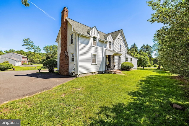 view of side of property featuring a chimney, roof with shingles, a yard, and asphalt driveway