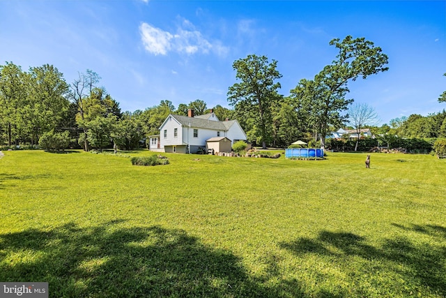 view of grassy yard featuring a swimming pool and view of wooded area