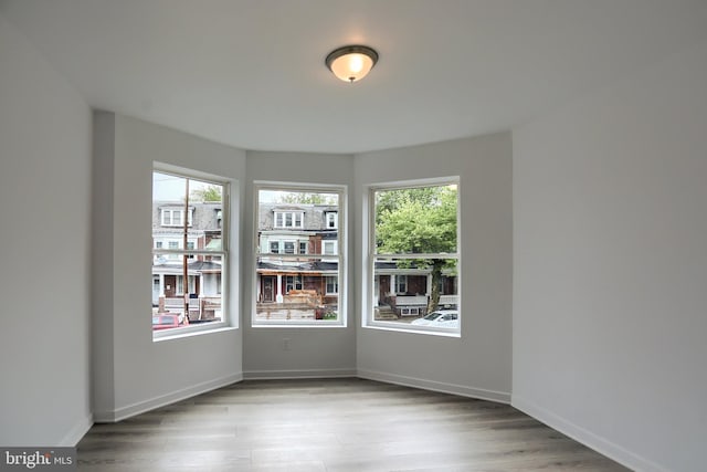 empty room with healthy amount of natural light, wood finished floors, and baseboards