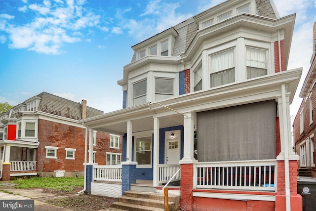 victorian home with covered porch, mansard roof, and brick siding