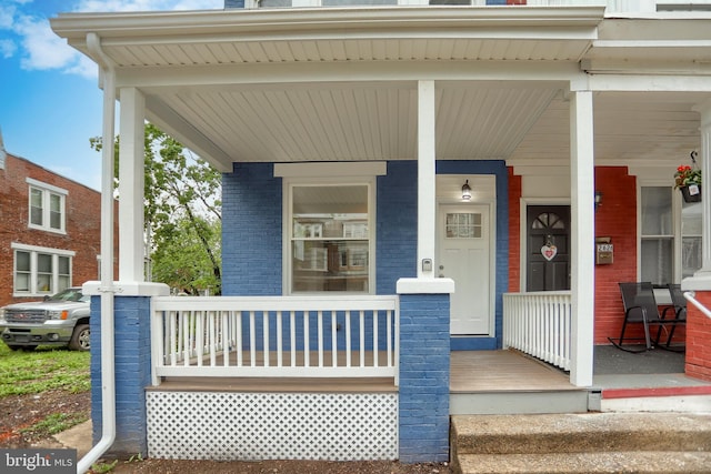 doorway to property featuring a porch and brick siding