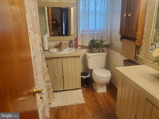 bathroom with vanity, toilet, wallpapered walls, and wood finished floors