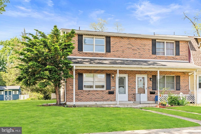 townhome / multi-family property featuring a front yard, covered porch, brick siding, a storage unit, and an outdoor structure