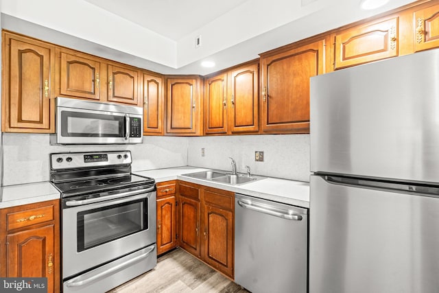 kitchen featuring appliances with stainless steel finishes, a sink, brown cabinets, and light countertops