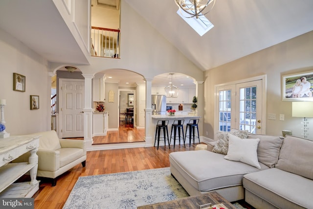 living room featuring light wood-style floors, high vaulted ceiling, ornate columns, and arched walkways