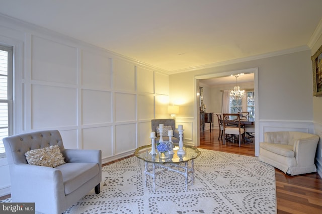 living area featuring a notable chandelier, ornamental molding, a decorative wall, and wood finished floors